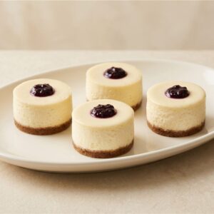 Creamy individual cheesecake with a biscuit crumb base and boysenberry topping. Serving presentation.