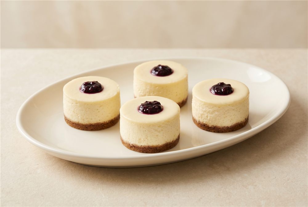 Creamy individual cheesecake with a biscuit crumb base and boysenberry topping. Serving presentation.