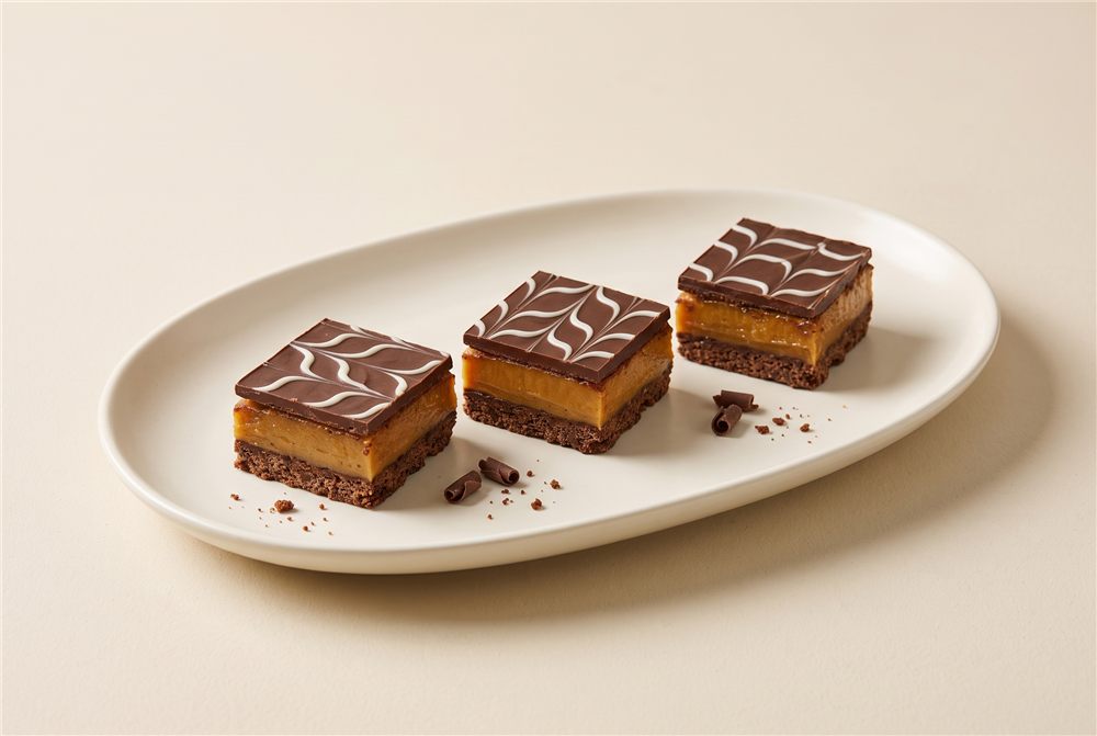 A rich mini slice with a chocolate base, caramel centre and feathered chocolate topping. Serving presentation.